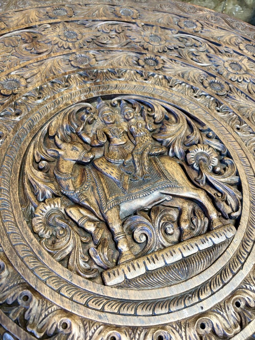 A large circular dark teak Anglo-Indian table featuring a deeply hand-carved floral top supported by three carved elephant legs with white tusks. View VII