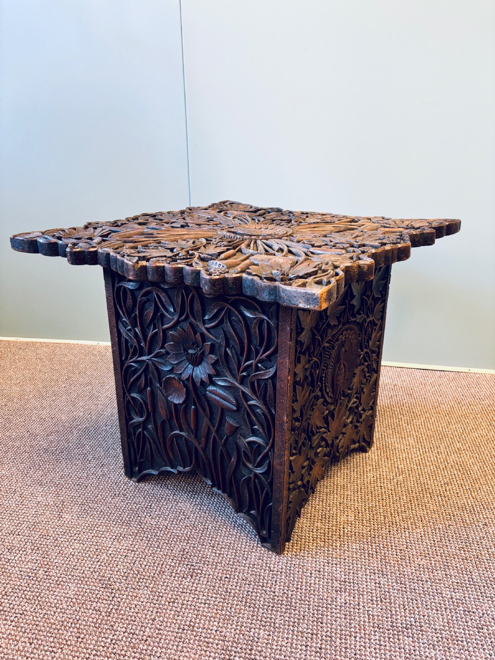 A square dark hardwood side table featuring intricate relief carvings of lotus flowers and foliage across the top and side panels.