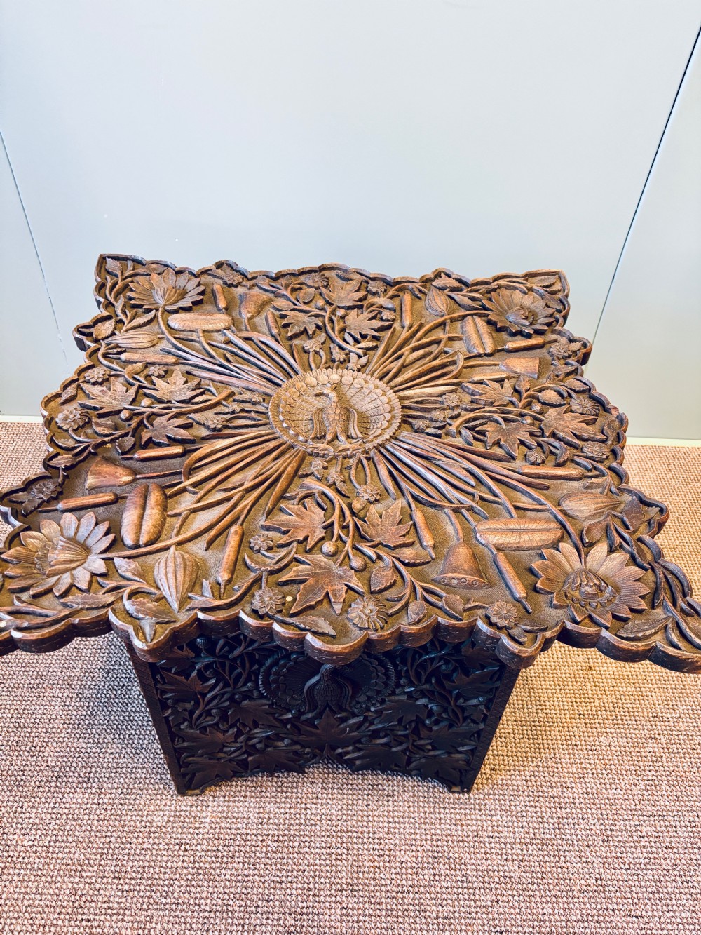 A square dark hardwood side table featuring intricate relief carvings of lotus flowers and foliage across the top and side panels. View V