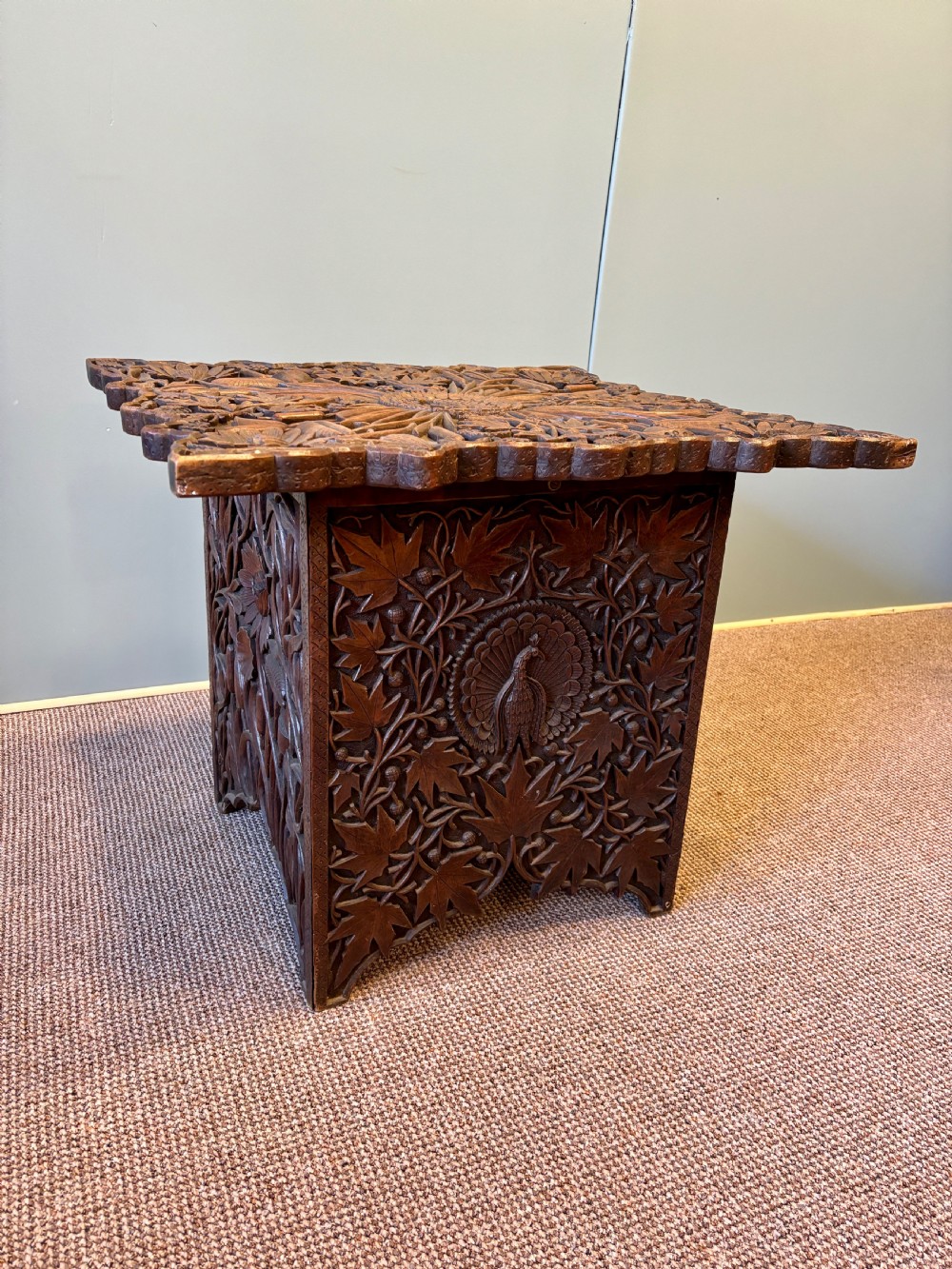 A square dark hardwood side table featuring intricate relief carvings of lotus flowers and foliage across the top and side panels. View VI