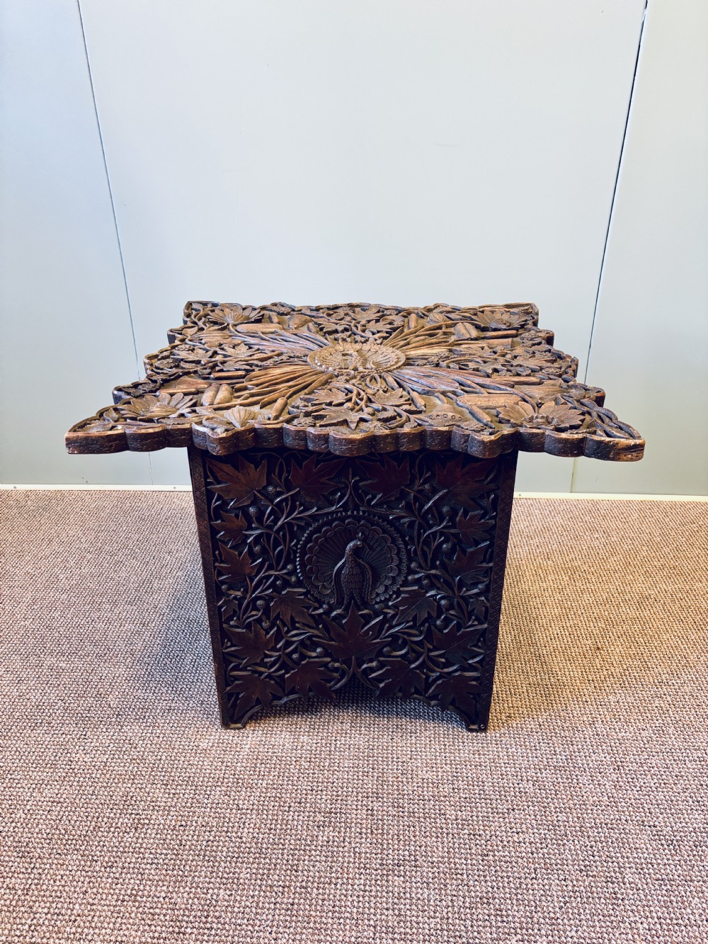 A square dark hardwood side table featuring intricate relief carvings of lotus flowers and foliage across the top and side panels. View VII
