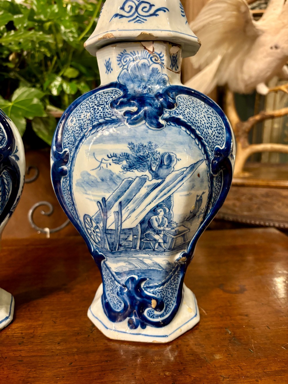 A pair of octagonal 18th-century Dutch Delftware lidded vases featuring blue hand-painted scenes within scrollwork cartouches and topped with bird finials. View II