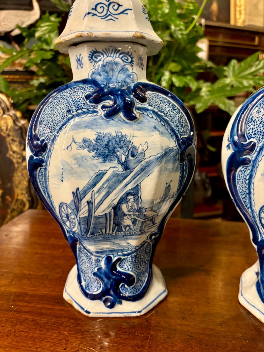 A pair of octagonal 18th-century Dutch Delftware lidded vases featuring blue hand-painted scenes within scrollwork cartouches and topped with bird finials. View III