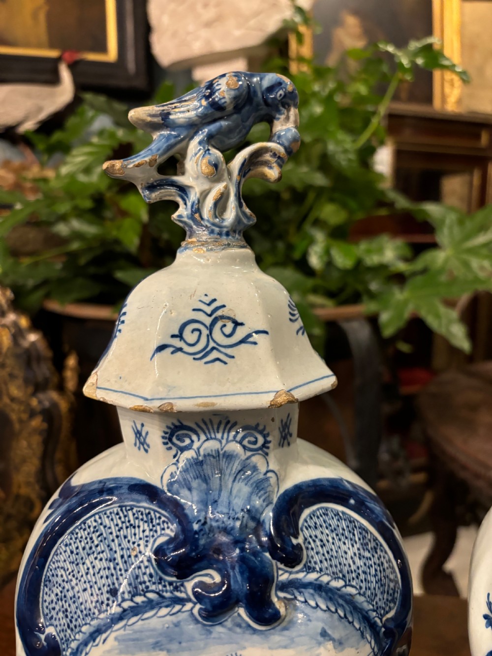 A pair of octagonal 18th-century Dutch Delftware lidded vases featuring blue hand-painted scenes within scrollwork cartouches and topped with bird finials. View V