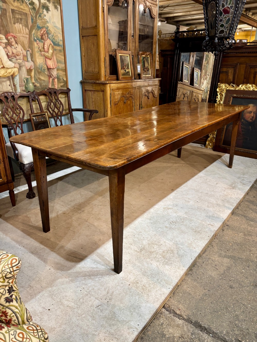 A long 19th-century French farmhouse dining table in warm brown wood with a polished plank top and square tapered legs.