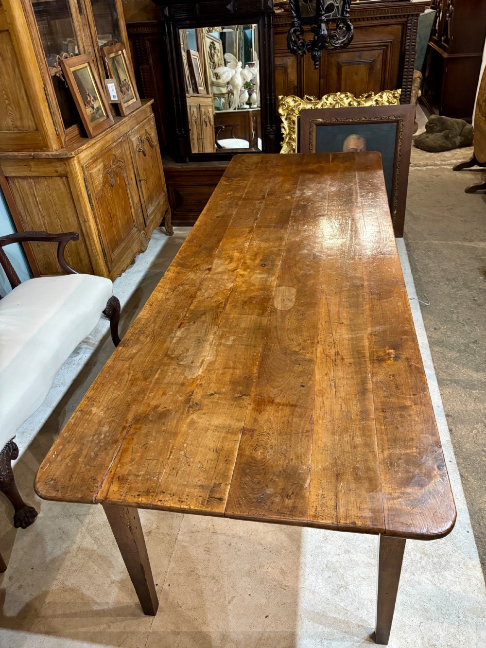 A long 19th-century French farmhouse dining table in warm brown wood with a polished plank top and square tapered legs. View V