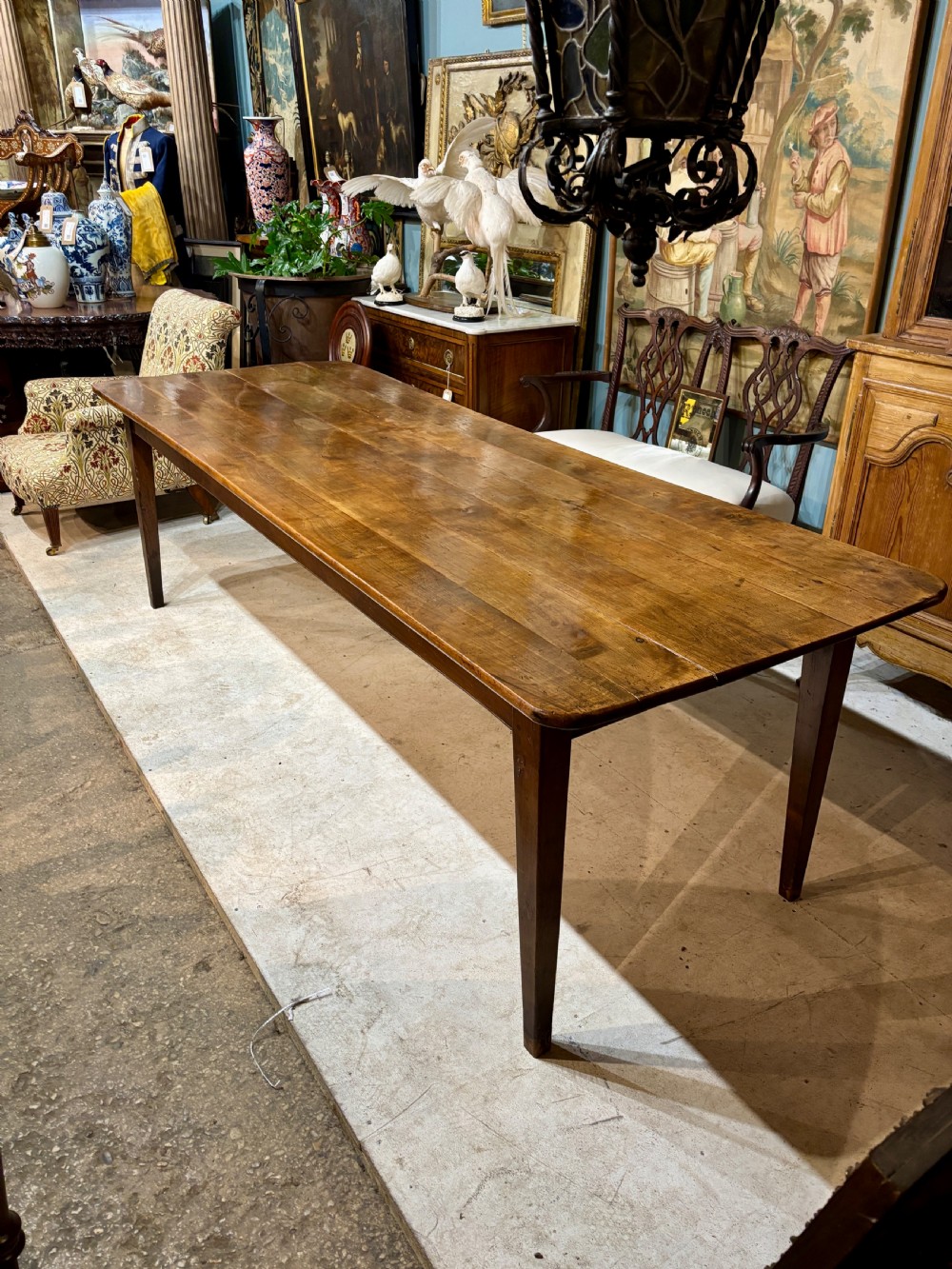 A long 19th-century French farmhouse dining table in warm brown wood with a polished plank top and square tapered legs. View X
