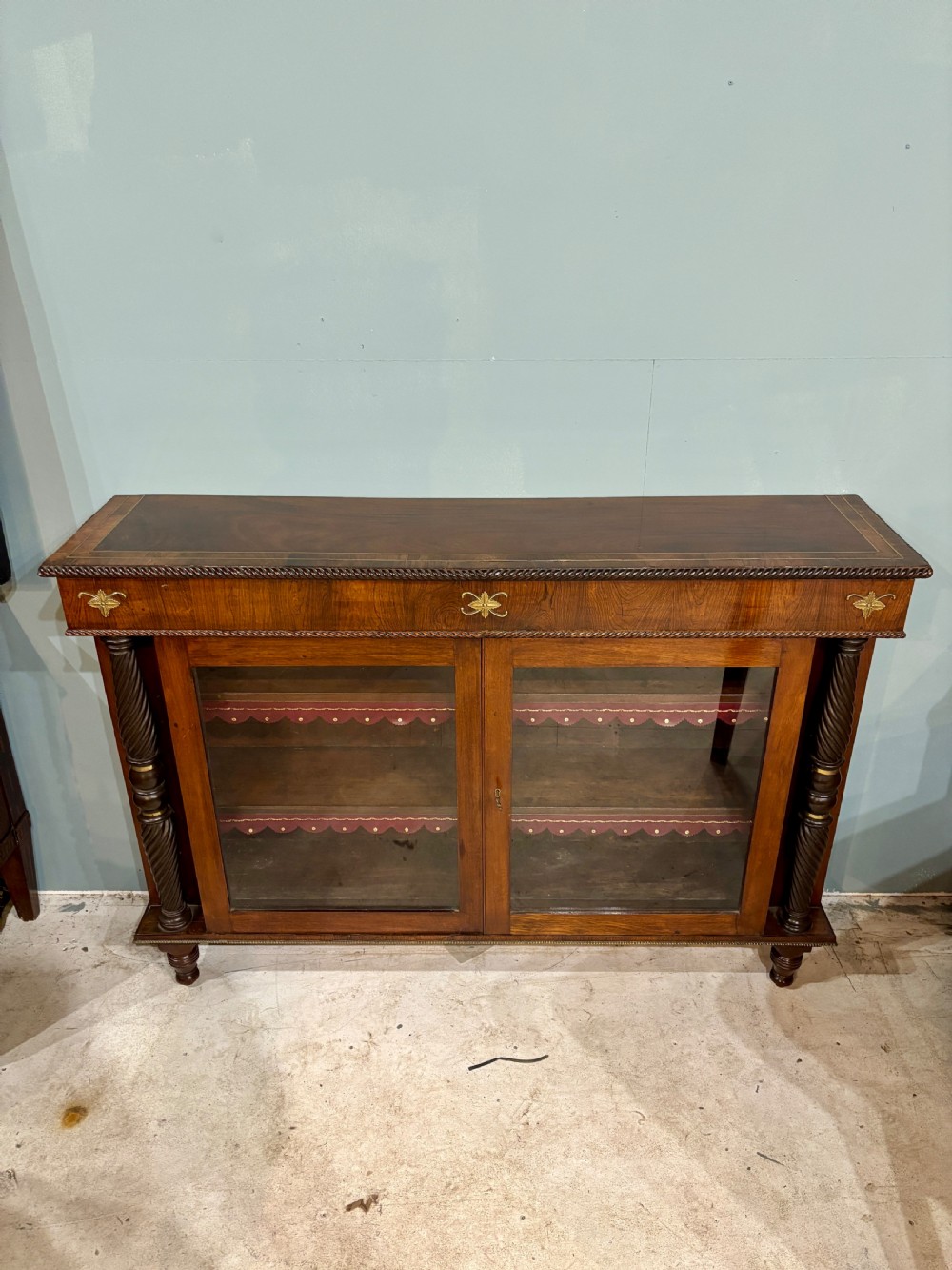 A 19th-century low rosewood bookcase featuring twin glazed doors flanked by spiral columns and decorated with brass rosette mounts. View V