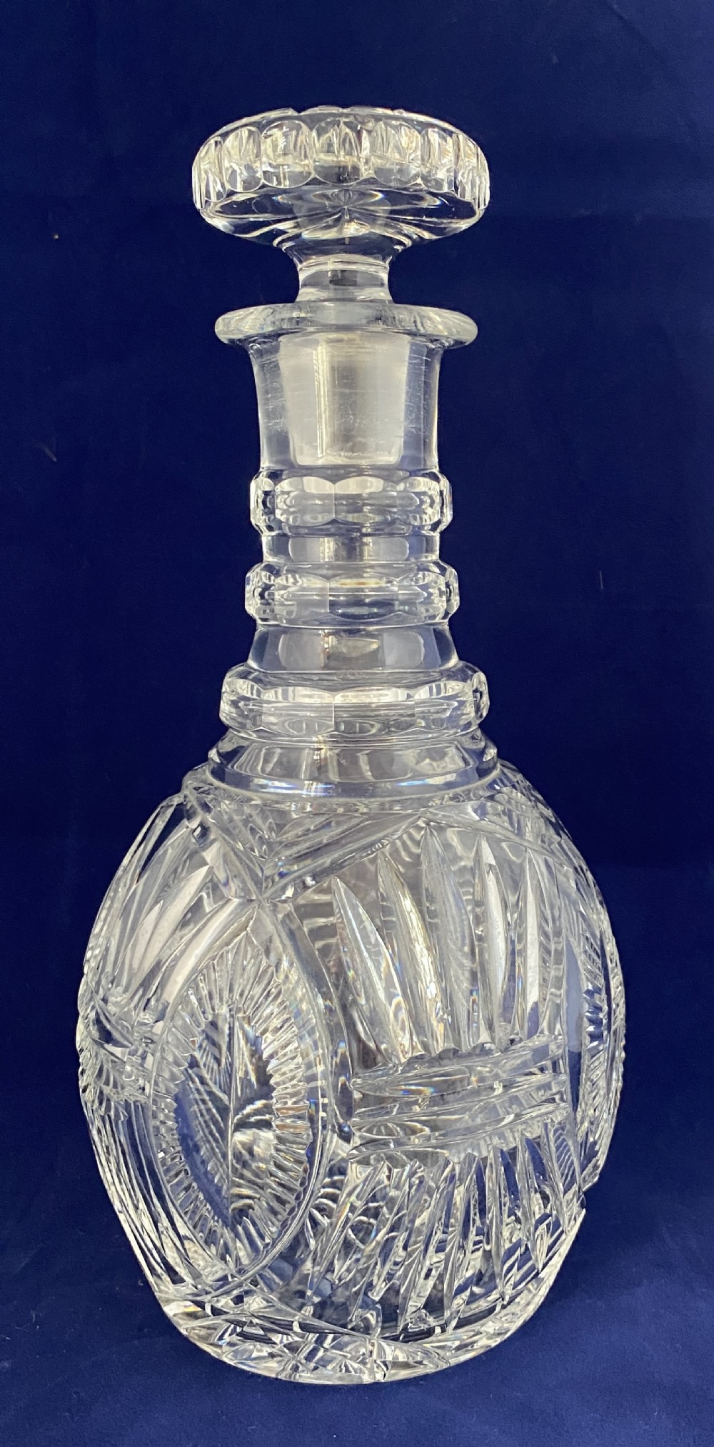 A clear cut crystal decanter featuring a spherical body with geometric diamond facets, three neck rings, and a matching rounded stopper.