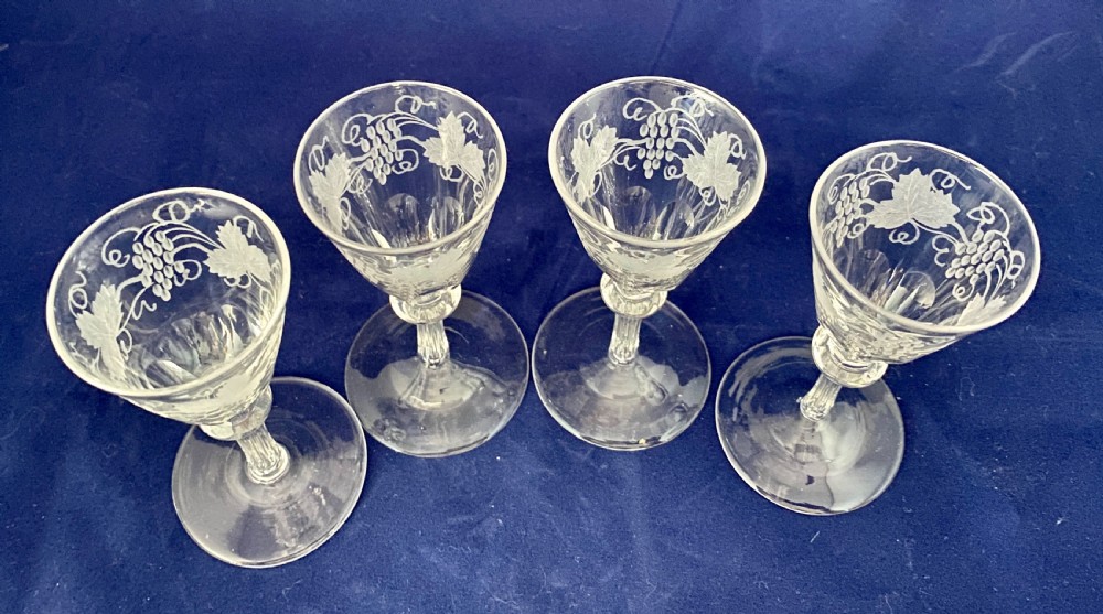 A set of four clear Victorian glass cordial glasses featuring acid-etched grape and vine motifs around the bowls and faceted stems. View II