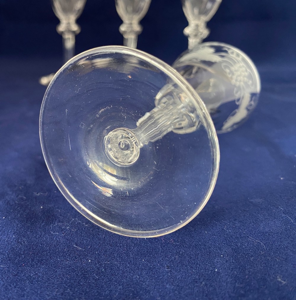 A set of four clear Victorian glass cordial glasses featuring acid-etched grape and vine motifs around the bowls and faceted stems. View III