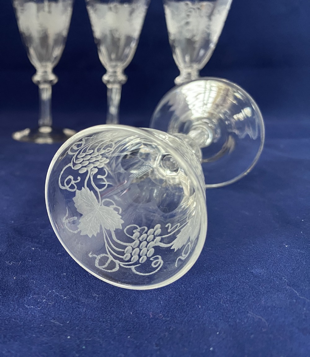A set of four clear Victorian glass cordial glasses featuring acid-etched grape and vine motifs around the bowls and faceted stems. View IV