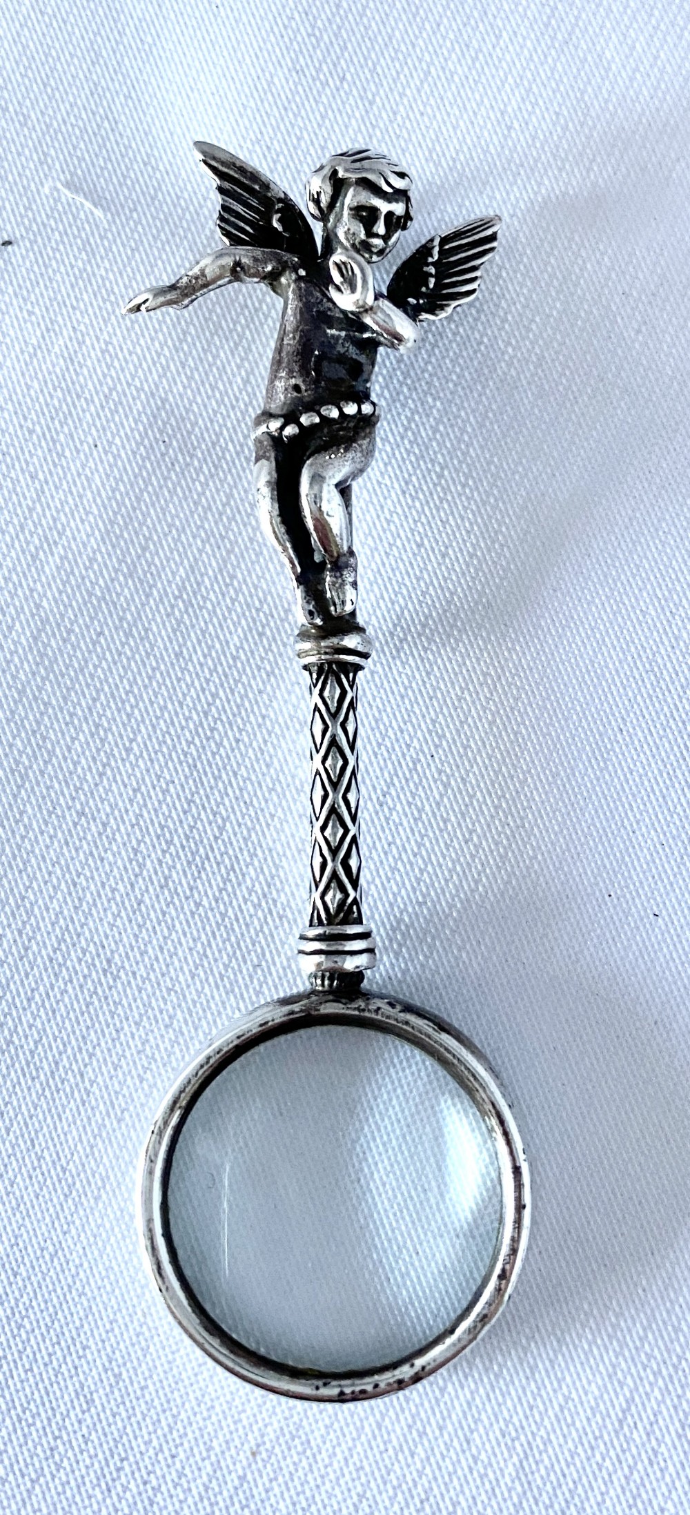 An antique silver-mounted magnifying glass featuring a sculpted cherub handle with a diamond-textured stem above a circular glass lens.
