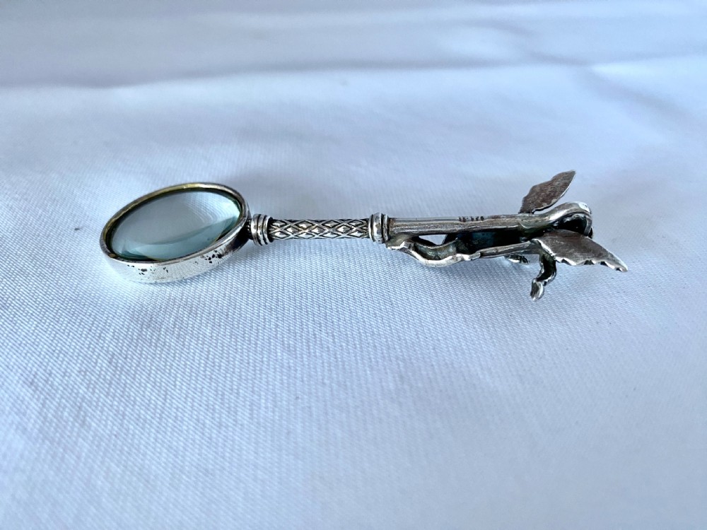An antique silver-mounted magnifying glass featuring a sculpted cherub handle with a diamond-textured stem above a circular glass lens. View IV