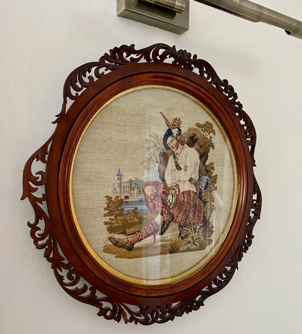 A circular Victorian woolwork picture depicting a seated Scottish Highlander in a kilt, housed in a pierced carved wooden frame. View II