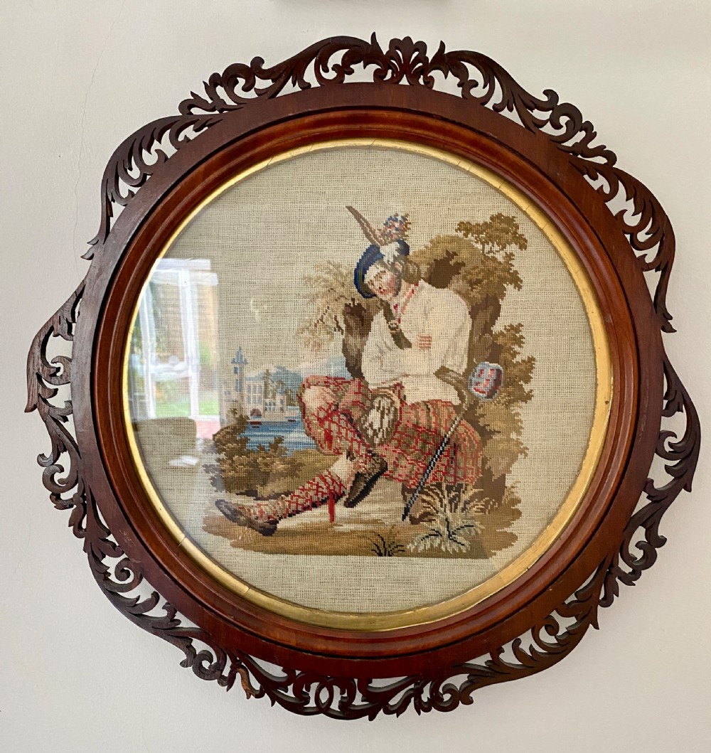 A circular Victorian woolwork picture depicting a seated Scottish Highlander in a kilt, housed in a pierced carved wooden frame. View IV
