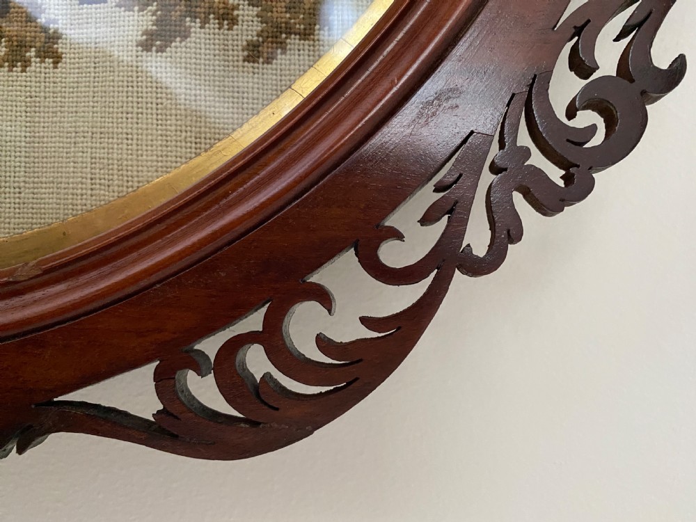 A circular Victorian woolwork picture depicting a seated Scottish Highlander in a kilt, housed in a pierced carved wooden frame. View V
