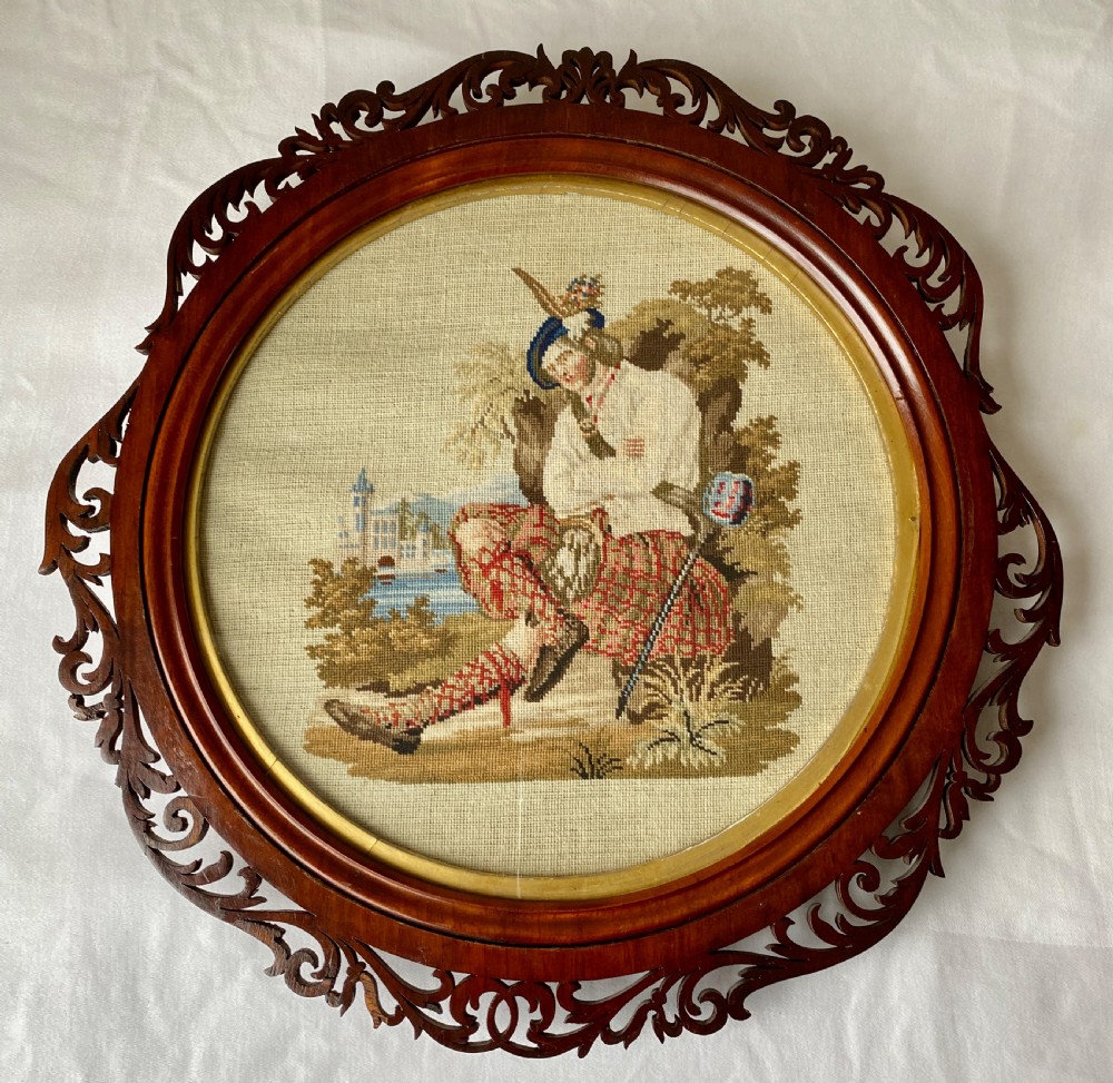 A circular Victorian woolwork picture depicting a seated Scottish Highlander in a kilt, housed in a pierced carved wooden frame. View VIII