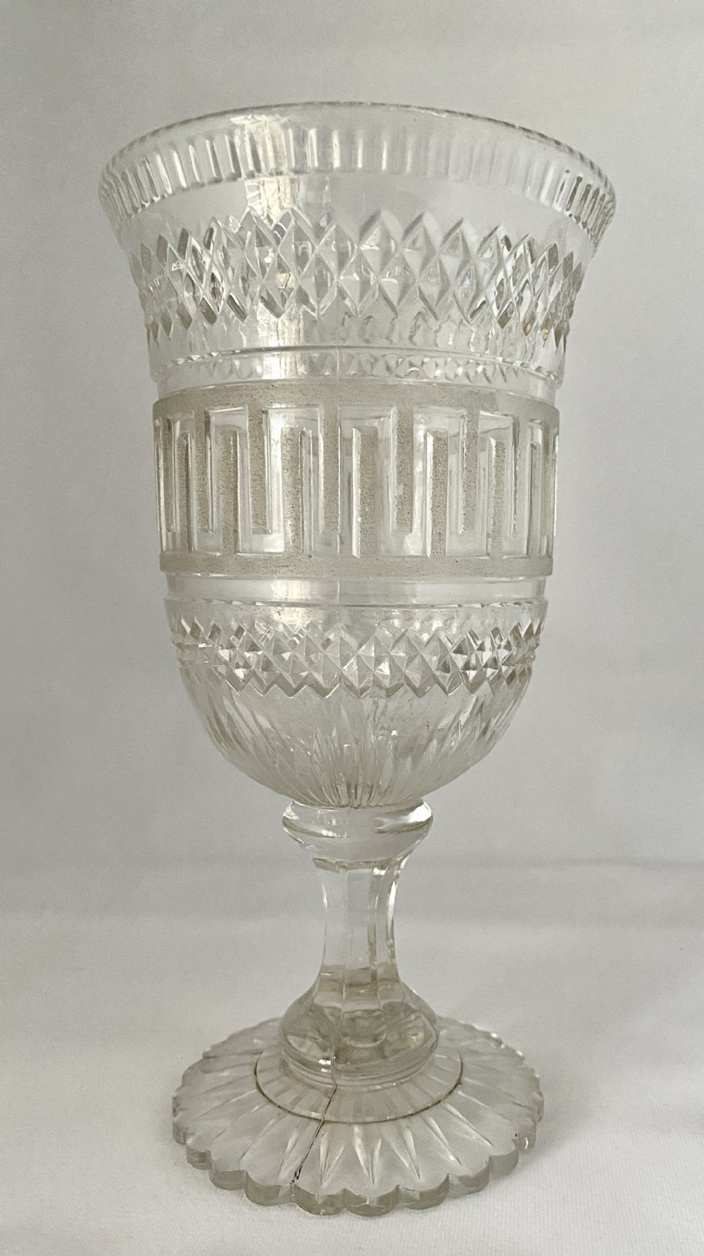 A clear glass Victorian celery vase featuring flared rim, diamond cut bands, a Greek key motif, and a scalloped circular pedestal foot.