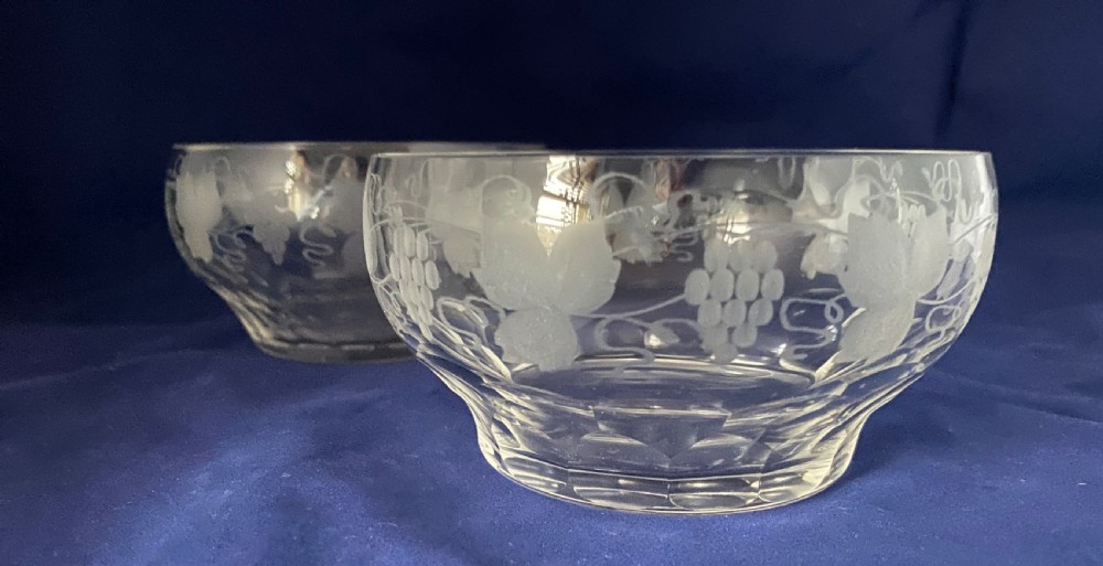 A pair of clear Victorian glass finger bowls with etched grape and vine motifs around the body and faceted cutting near the lower base.
