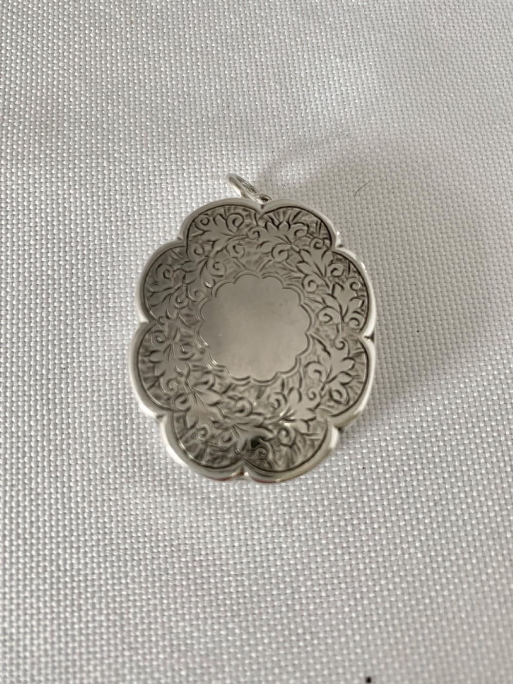 An antique Victorian sterling silver vinaigrette with a scalloped edge, foliate engraving, an unengraved central cartouche, and a suspension ring.