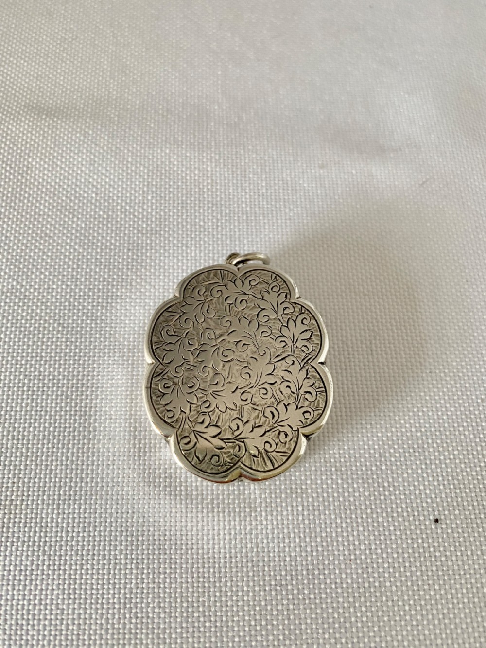 An antique Victorian sterling silver vinaigrette with a scalloped edge, foliate engraving, an unengraved central cartouche, and a suspension ring. View II