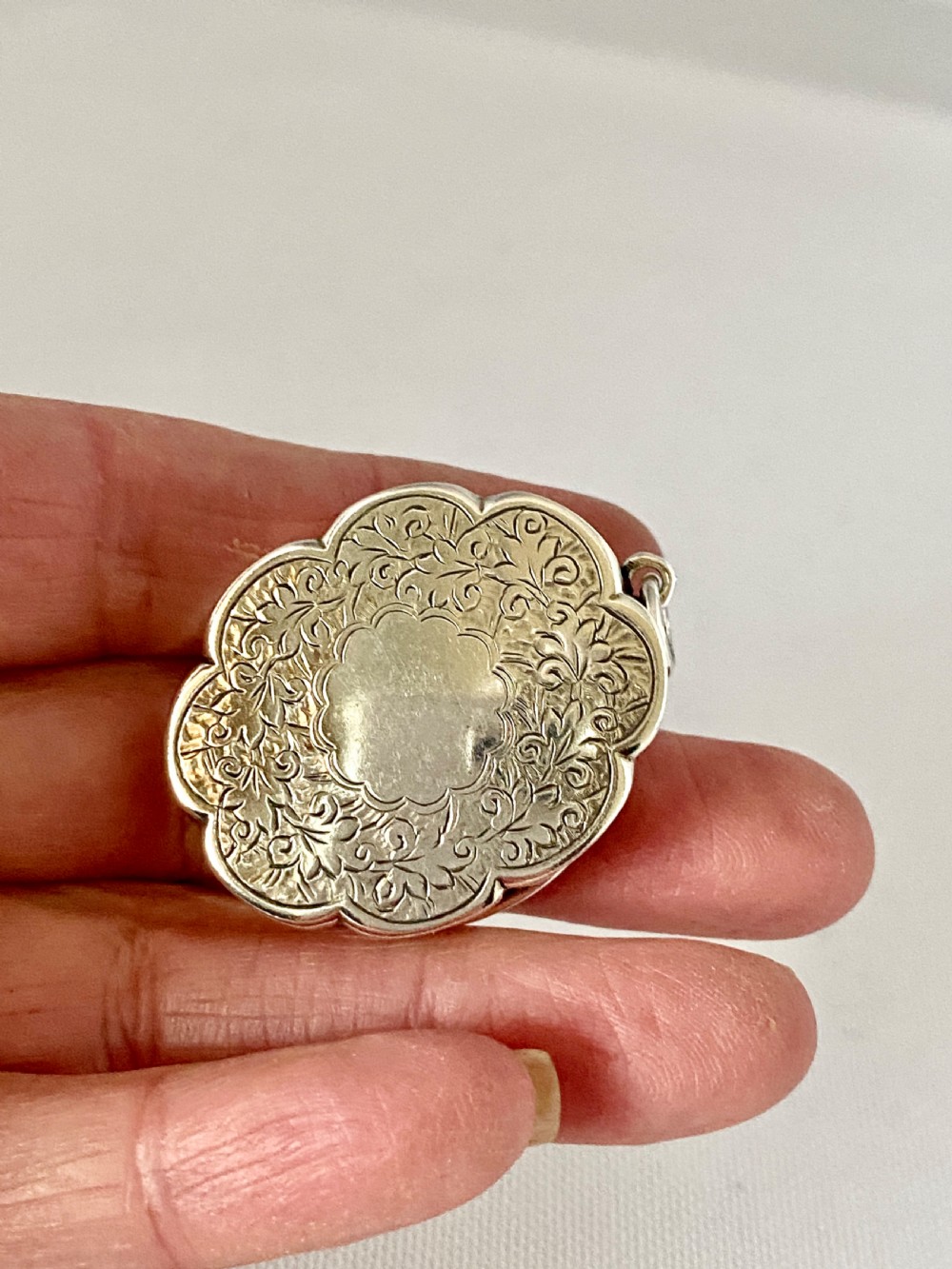 An antique Victorian sterling silver vinaigrette with a scalloped edge, foliate engraving, an unengraved central cartouche, and a suspension ring. View III