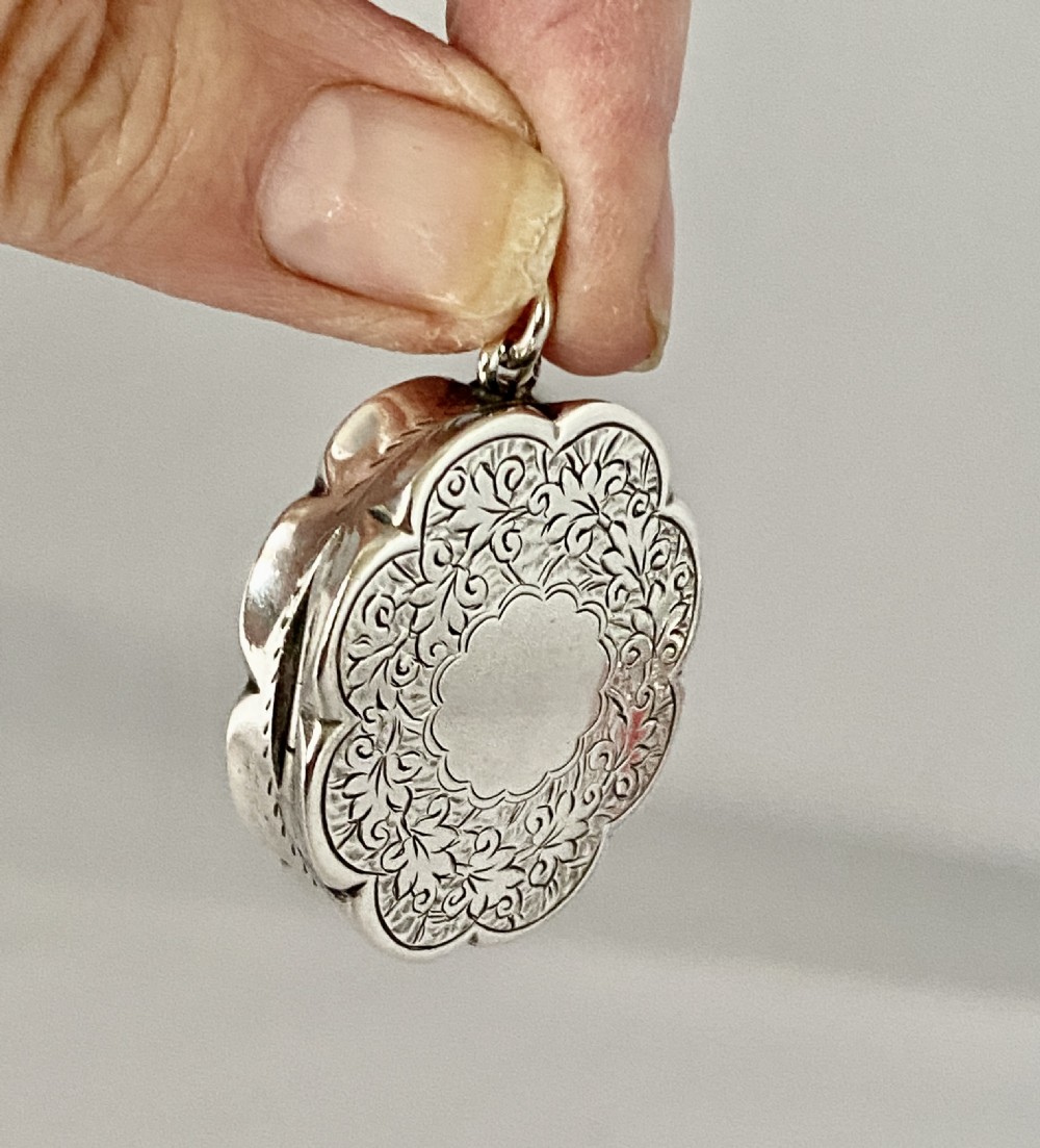 An antique Victorian sterling silver vinaigrette with a scalloped edge, foliate engraving, an unengraved central cartouche, and a suspension ring. View IV