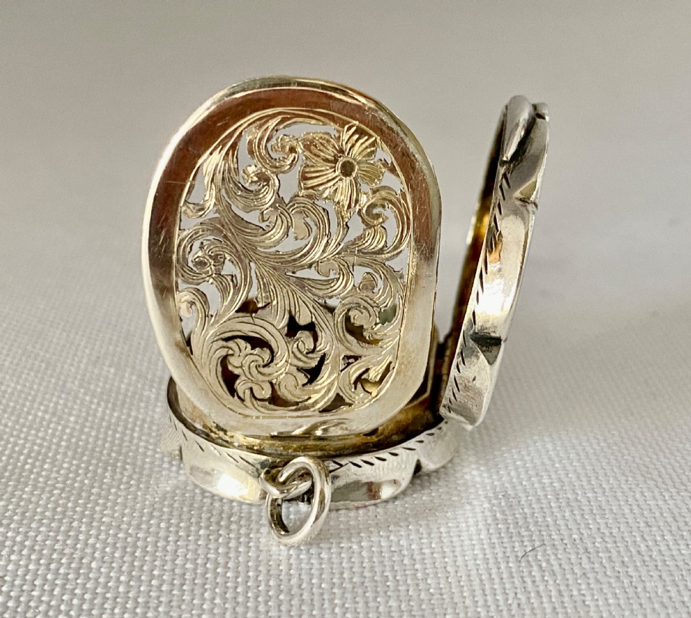 An antique Victorian sterling silver vinaigrette with a scalloped edge, foliate engraving, an unengraved central cartouche, and a suspension ring. View V