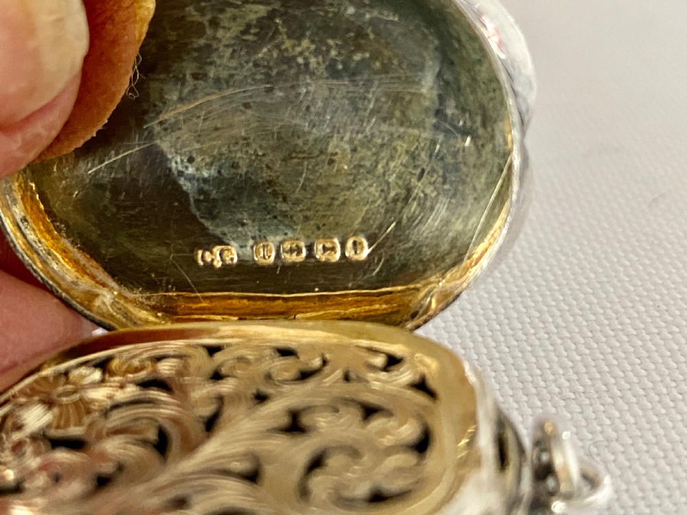 An antique Victorian sterling silver vinaigrette with a scalloped edge, foliate engraving, an unengraved central cartouche, and a suspension ring. View VII