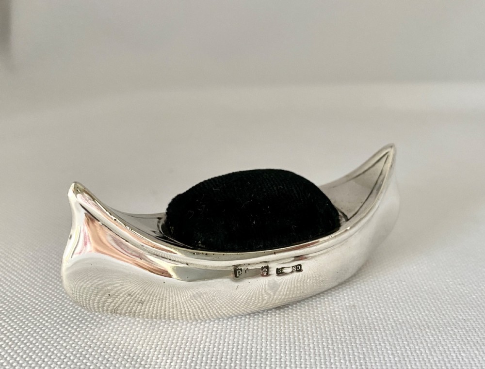 An Edwardian sterling silver pin cushion crafted in the shape of a canoe with a dark velvet insert and visible hallmarks on the exterior side.