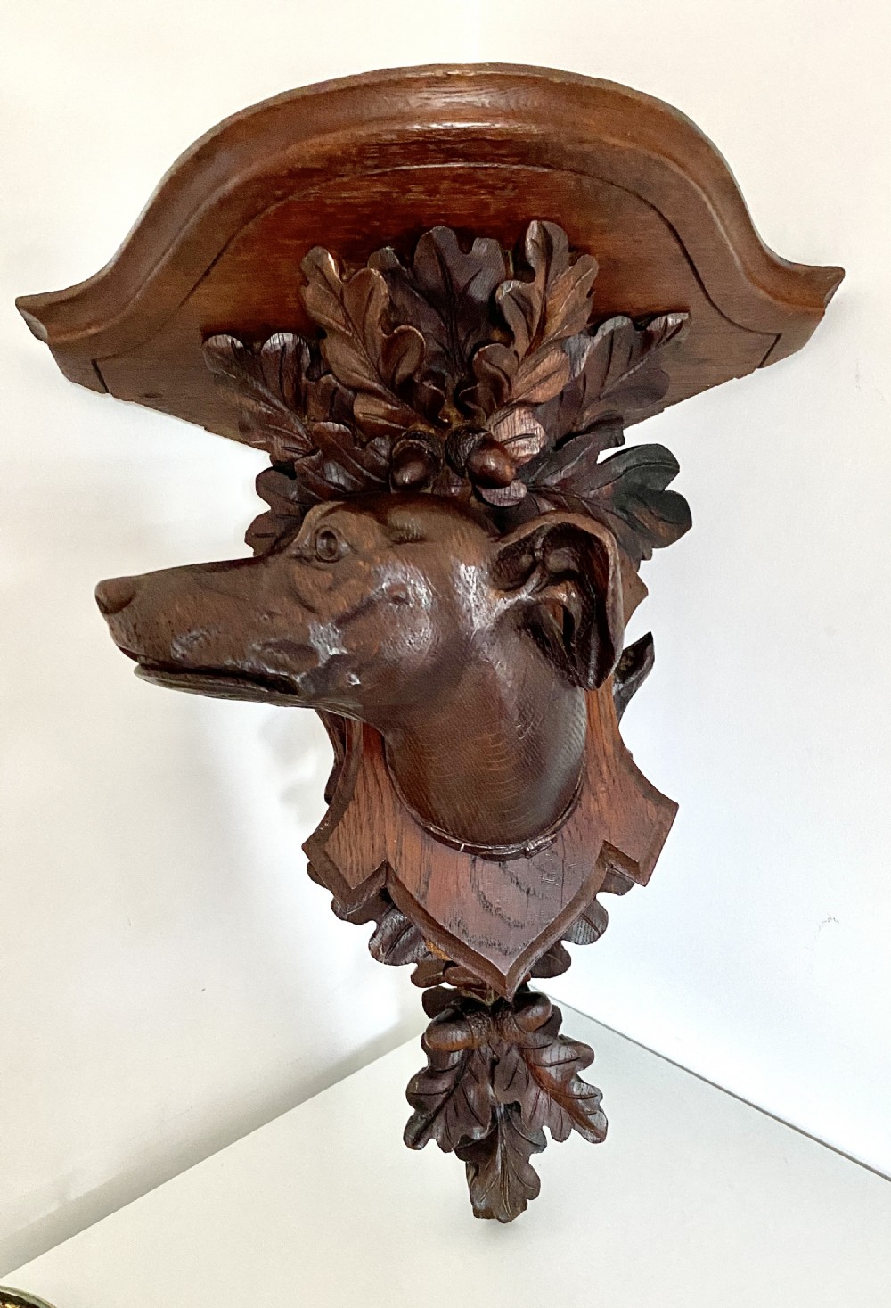 A Victorian carved oak corner bracket featuring a high-relief carved dog head surrounded by oak leaves and acorns beneath a curved corner shelf.
