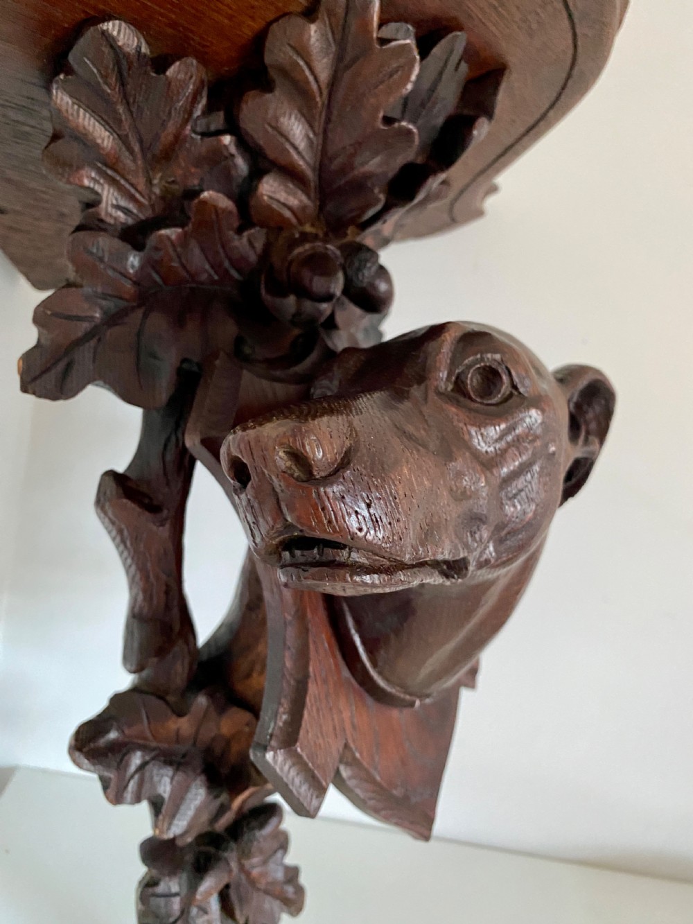 A Victorian carved oak corner bracket featuring a high-relief carved dog head surrounded by oak leaves and acorns beneath a curved corner shelf. View V