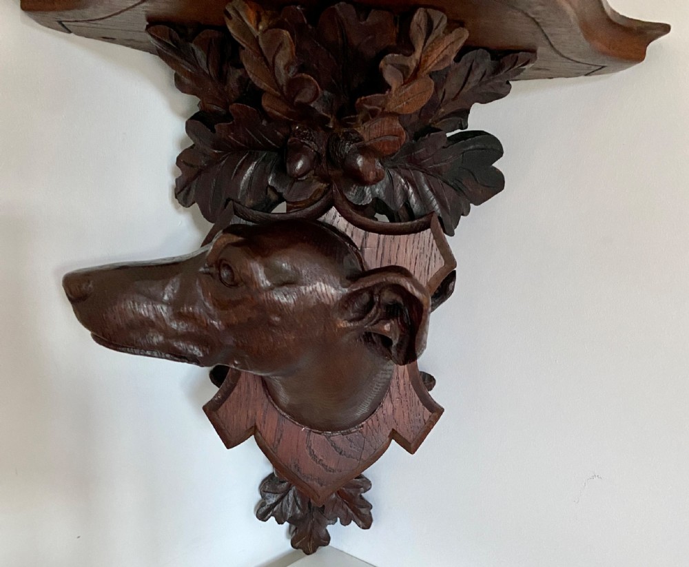 A Victorian carved oak corner bracket featuring a high-relief carved dog head surrounded by oak leaves and acorns beneath a curved corner shelf. View XI