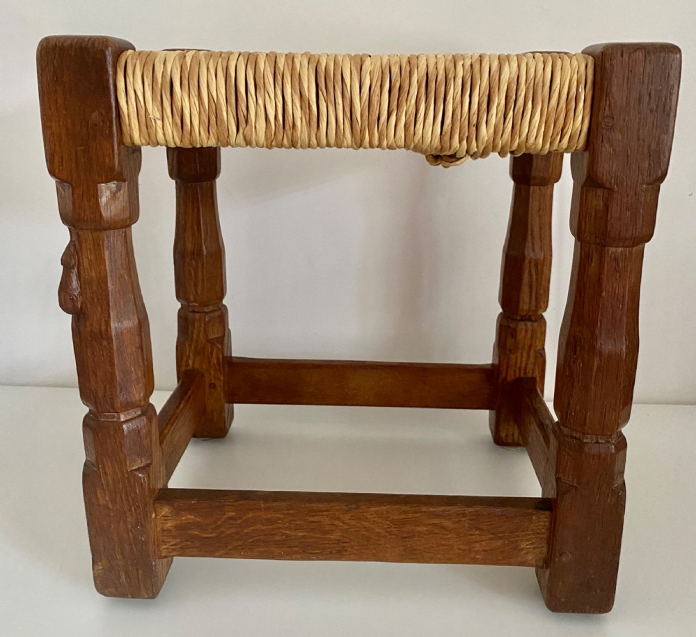 An English Arts and Crafts solid oak stool featuring a woven rush seat, turned faceted legs connected by rectangular stretchers, and a small carved mouse motif on one leg. View VIII