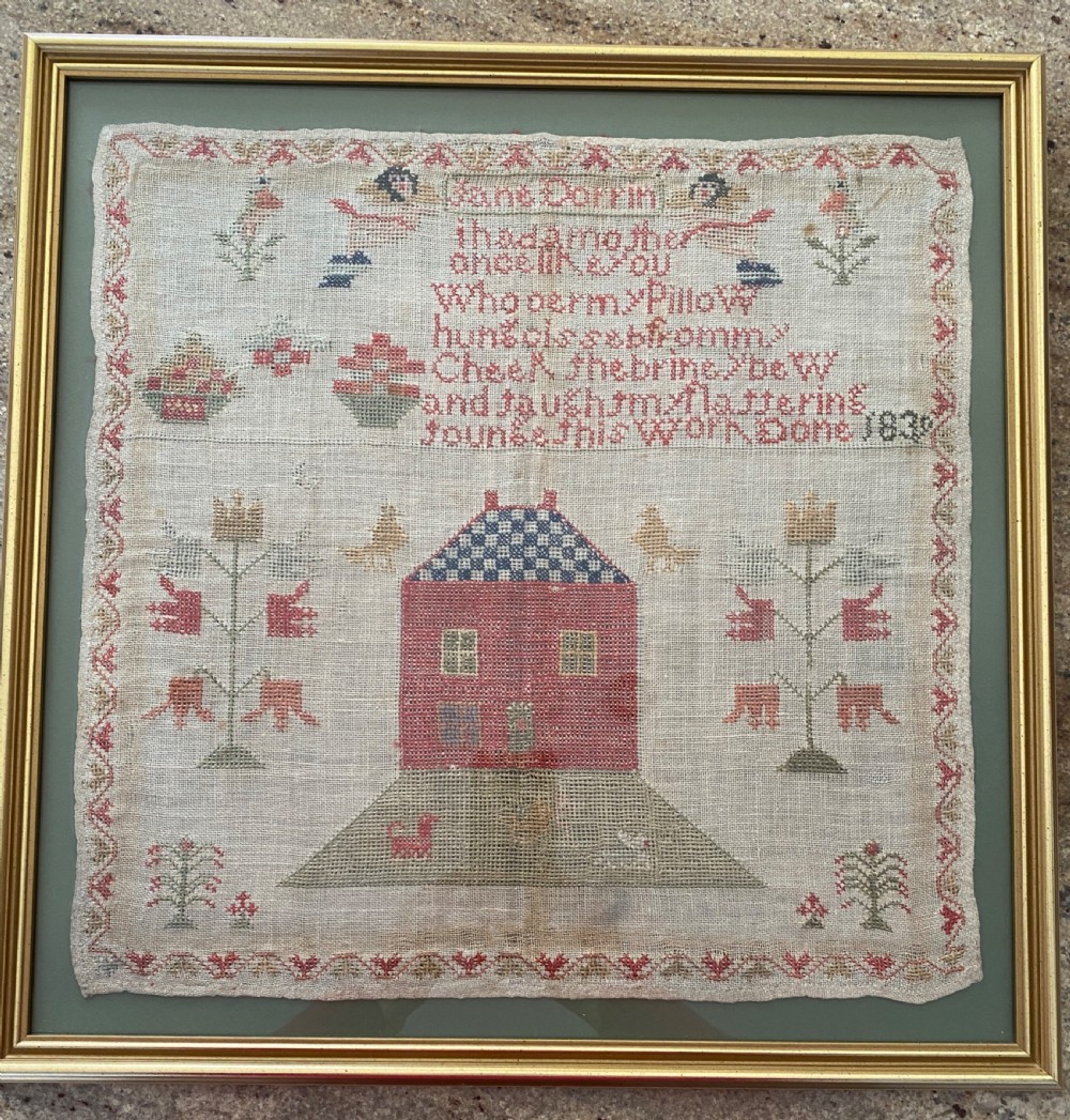 A framed 1839 Victorian needlework sampler featuring an embroidered verse, central house motif, floral trees, and the name Jane Dorrin on natural linen.