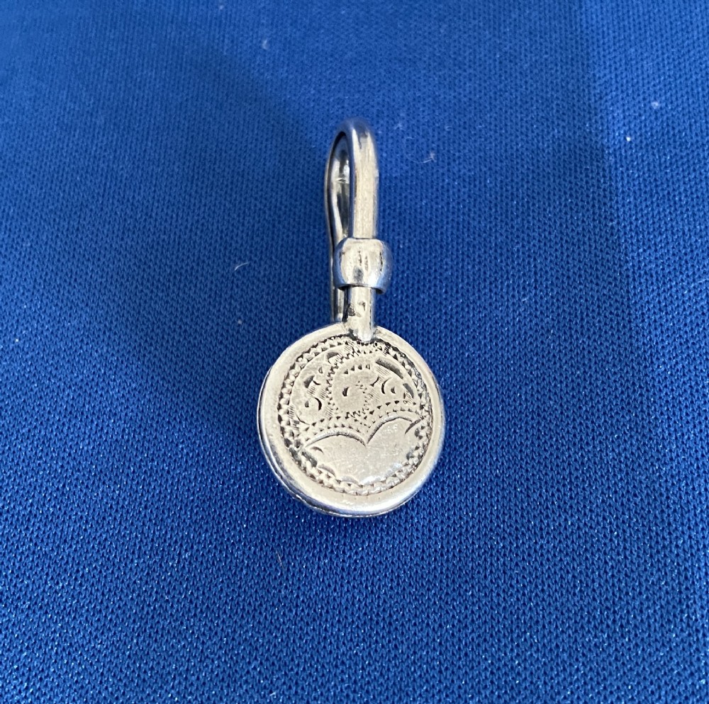 An Edwardian sterling silver napkin clip featuring a curved hook attached to a round engraved medallion.
