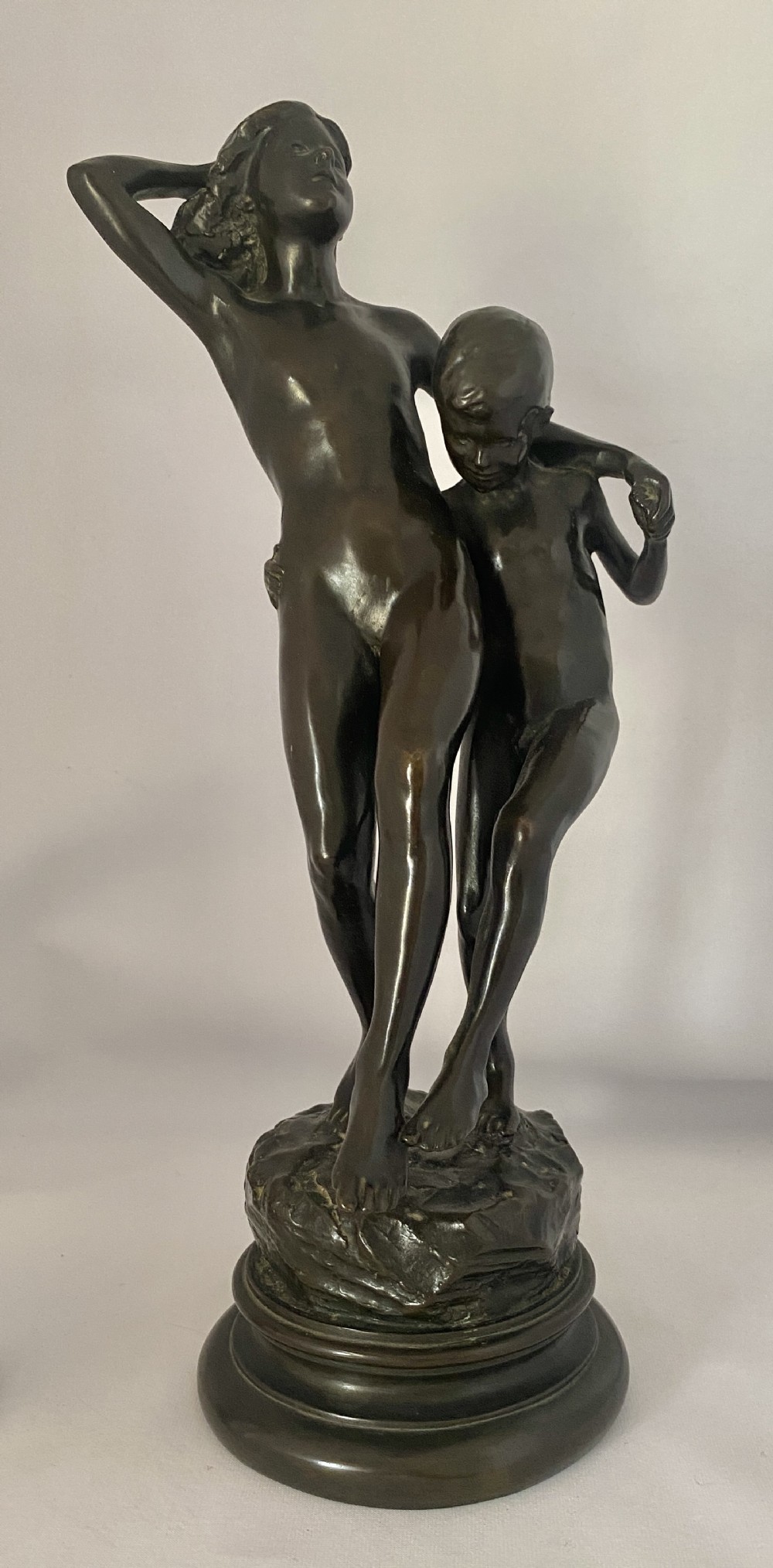 A dark patinated bronze figural group depicting two children in dynamic motion standing atop a moulded circular base.