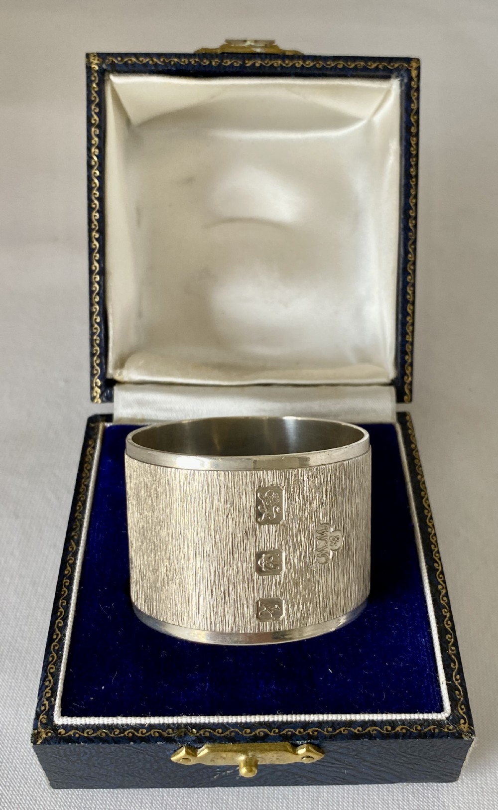 A cylindrical sterling silver napkin ring featuring a textured bark-effect surface, smooth polished borders, and visible stamped British hallmarks.