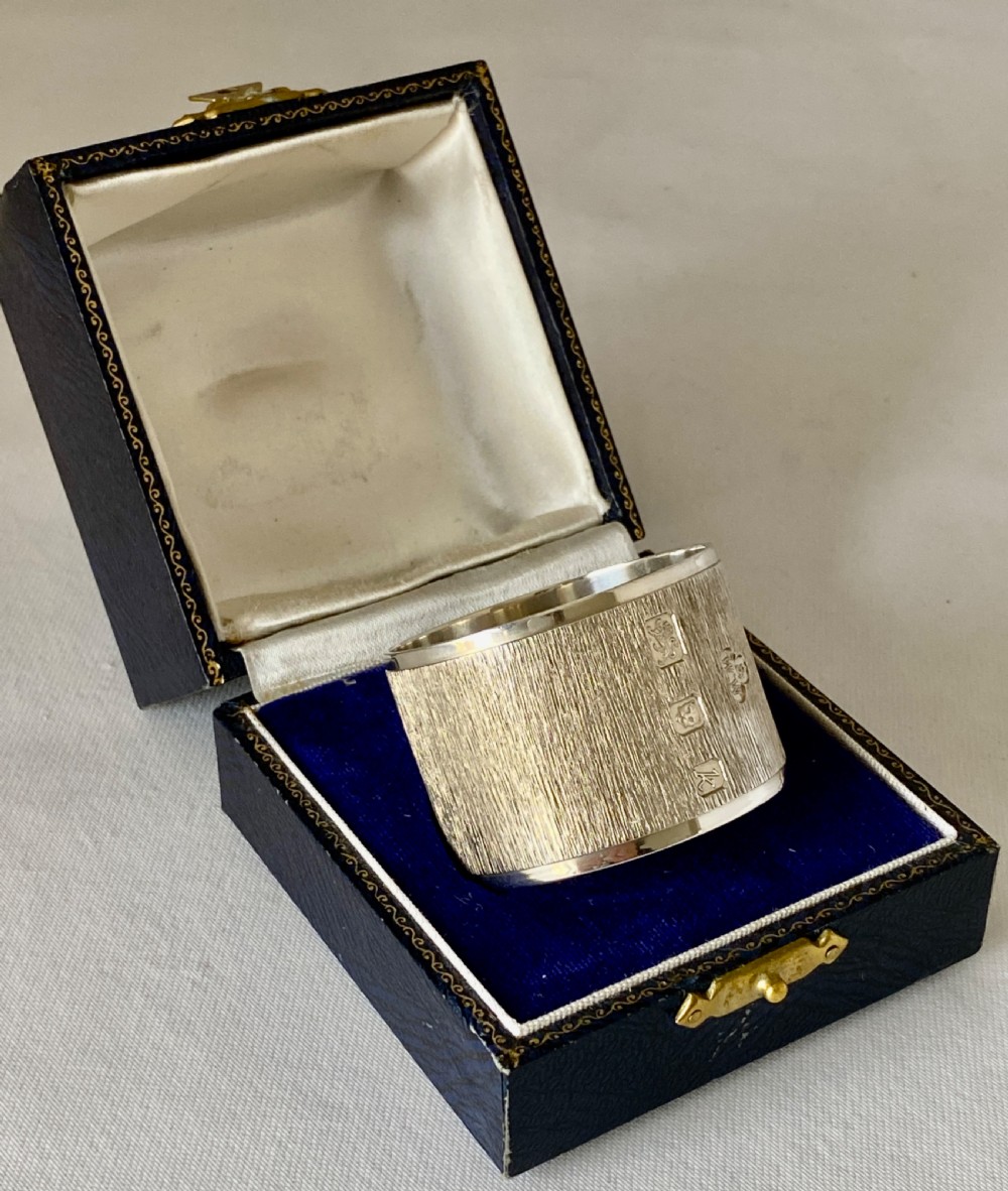 A cylindrical sterling silver napkin ring featuring a textured bark-effect surface, smooth polished borders, and visible stamped British hallmarks. View II
