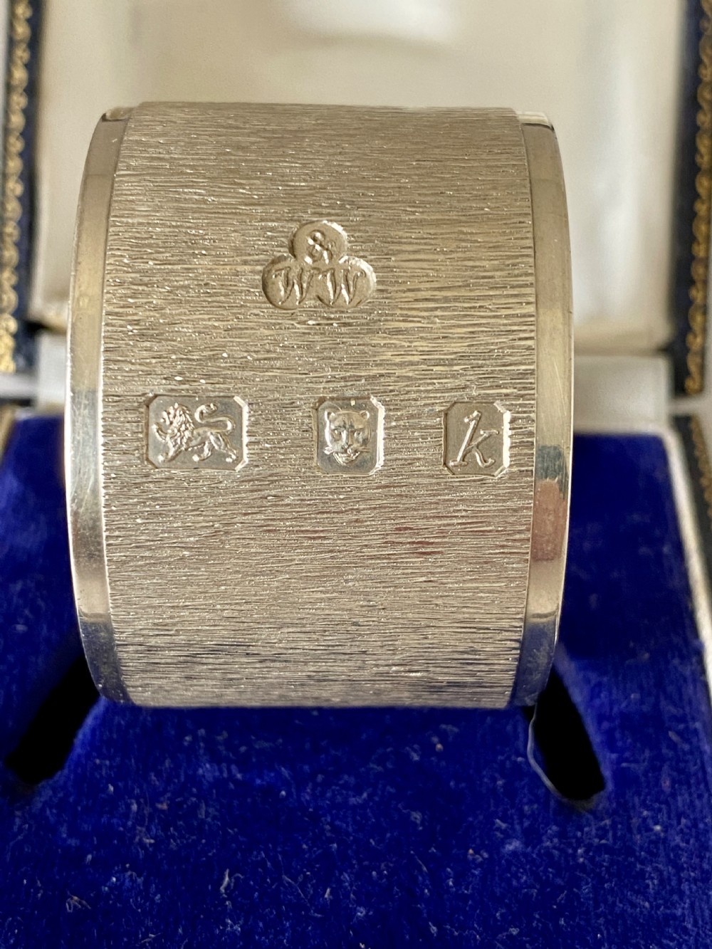 A cylindrical sterling silver napkin ring featuring a textured bark-effect surface, smooth polished borders, and visible stamped British hallmarks. View III