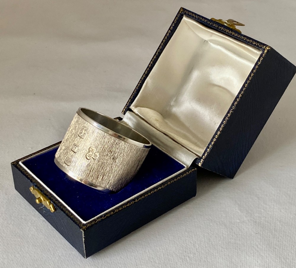 A cylindrical sterling silver napkin ring featuring a textured bark-effect surface, smooth polished borders, and visible stamped British hallmarks. View VII