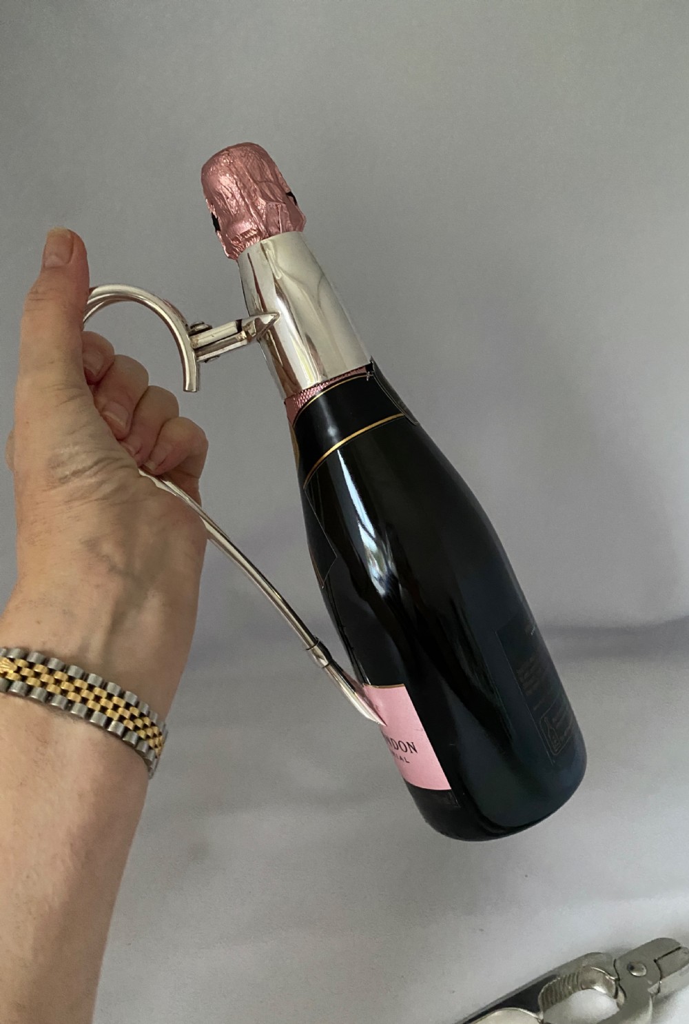 A silver-plated Art Deco champagne bottle pouring handle and matching champagne pliers set on a white fabric surface. View III