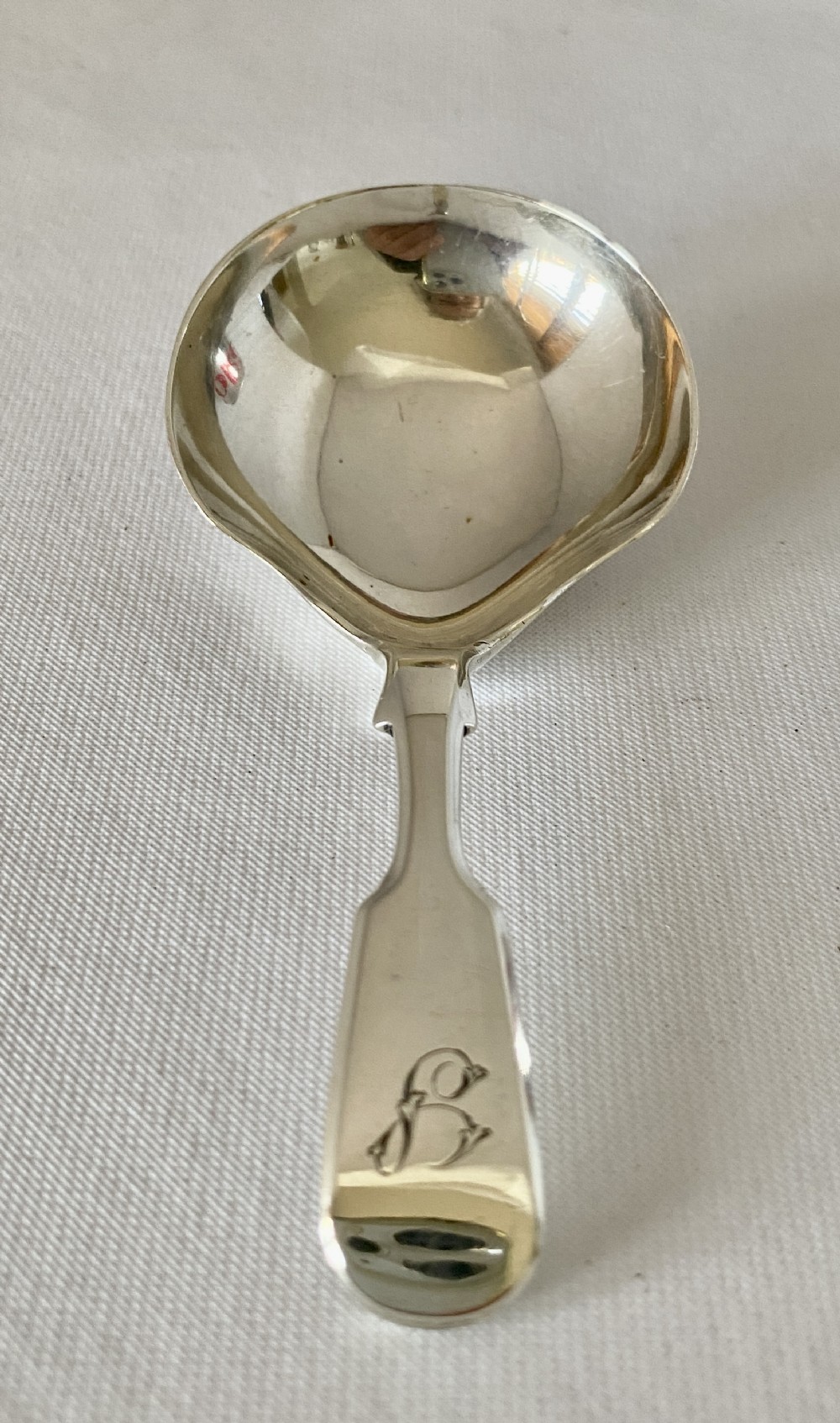 A Victorian sterling silver caddy spoon featuring a flared shovel-shaped bowl and a short handle engraved with a monogram.