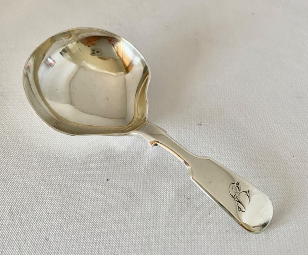 A Victorian sterling silver caddy spoon featuring a flared shovel-shaped bowl and a short handle engraved with a monogram. View II