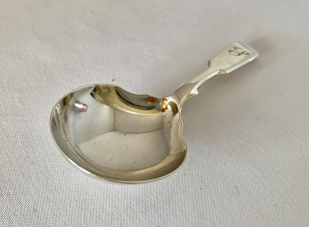A Victorian sterling silver caddy spoon featuring a flared shovel-shaped bowl and a short handle engraved with a monogram. View V