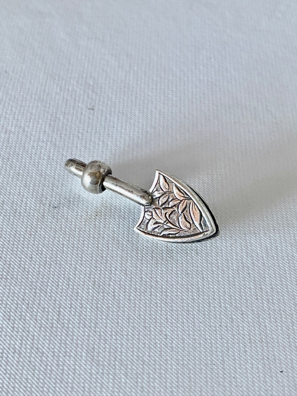 A solid sterling silver Victorian napkin clip featuring an engraved shield-shaped terminal and a sliding bar mechanism.