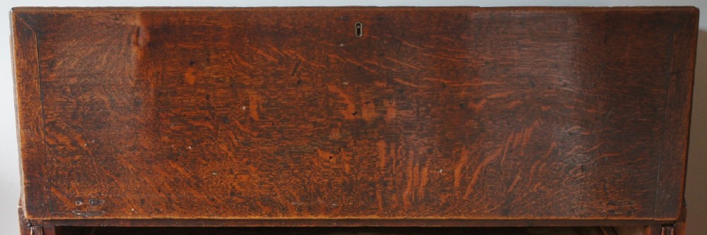 An 18th-century dark oak bureau featuring a slanted fall-front writing flap above four graduated drawers with brass handles. View IV