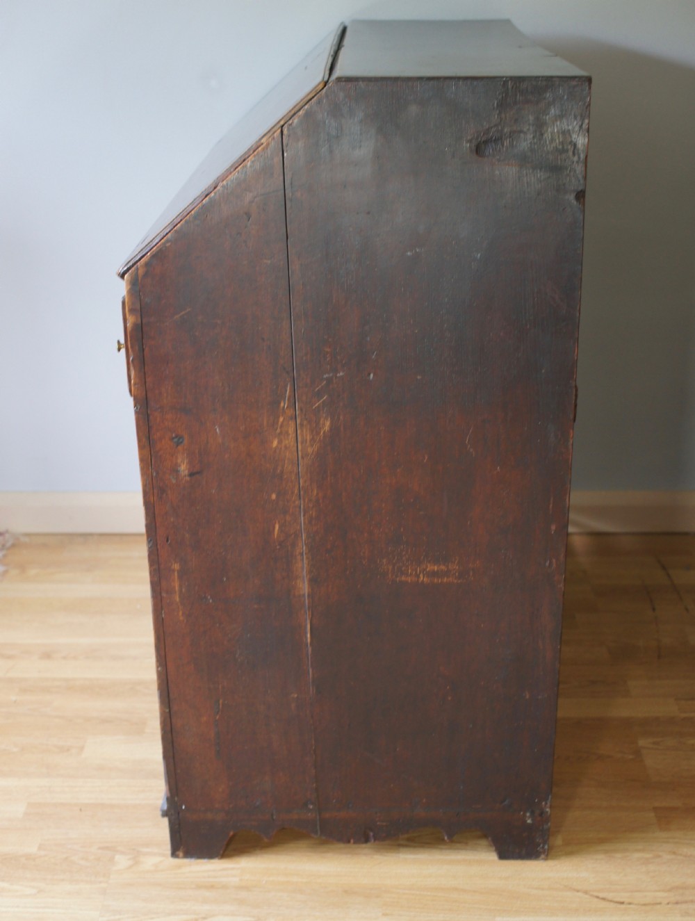 An 18th-century dark oak bureau featuring a slanted fall-front writing flap above four graduated drawers with brass handles. View VI