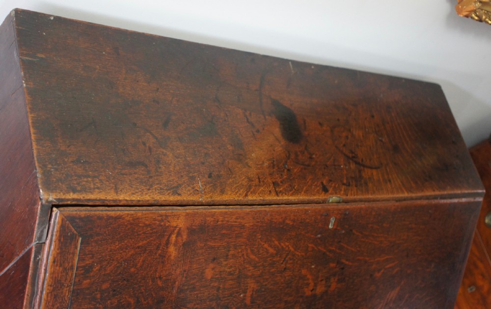 An 18th-century dark oak bureau featuring a slanted fall-front writing flap above four graduated drawers with brass handles. View IX